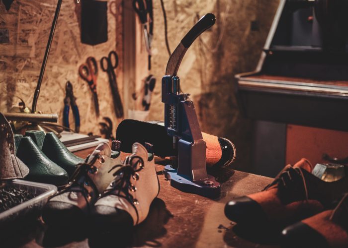 Machine tool on the table with shoes for making holes for laces at cobbler's workshop.